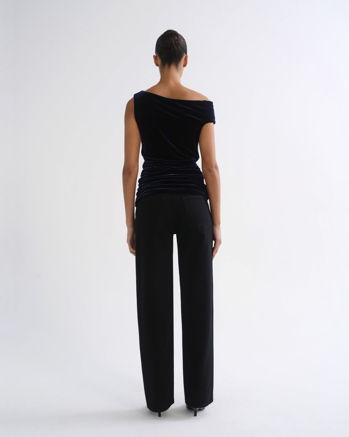 A model viewed from the back wearing a black off-the-shoulder velvet top and black wide-leg trousers against a plain white studio background.