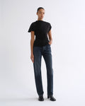 Woman wearing a black short sleeve top with dark indigo straight leg jeans on a grey background.