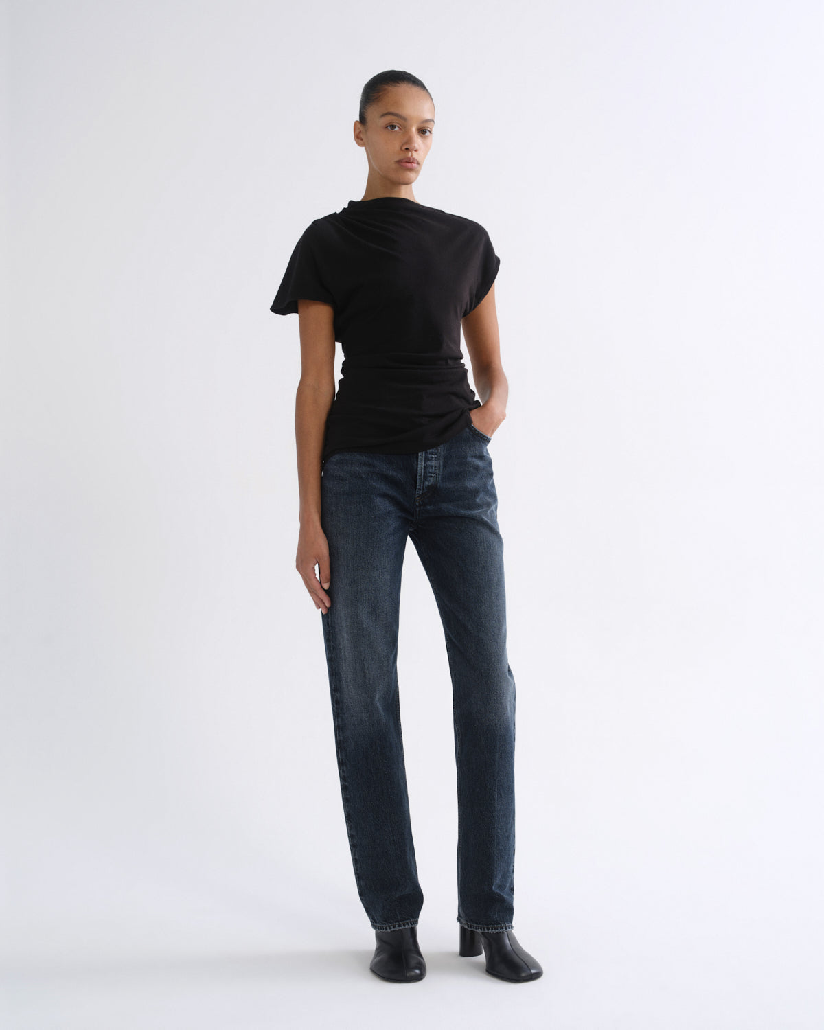 Woman wearing a black short sleeve top with dark indigo straight leg jeans on a grey background.