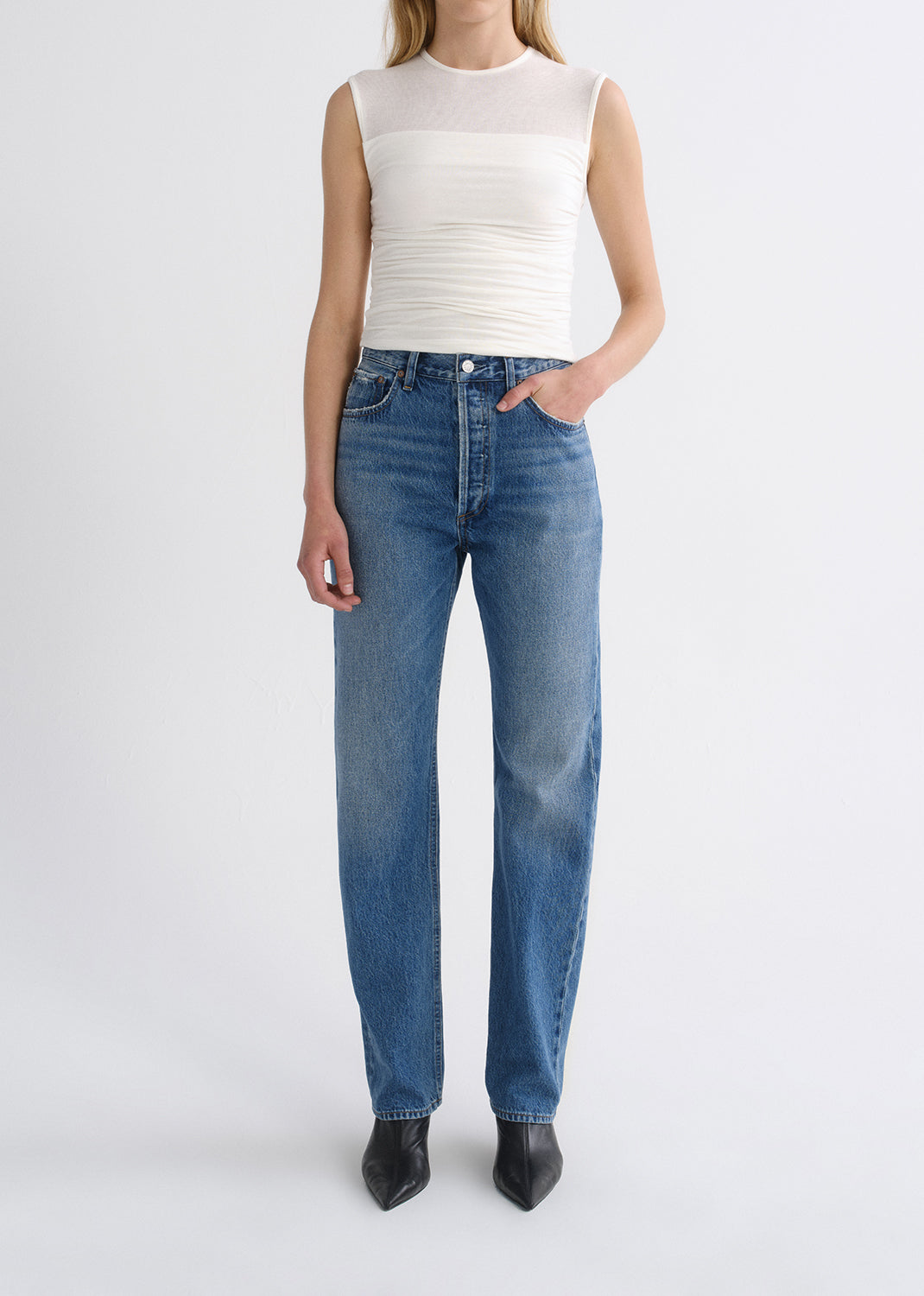 Person wearing white top with blue pants on a grey background