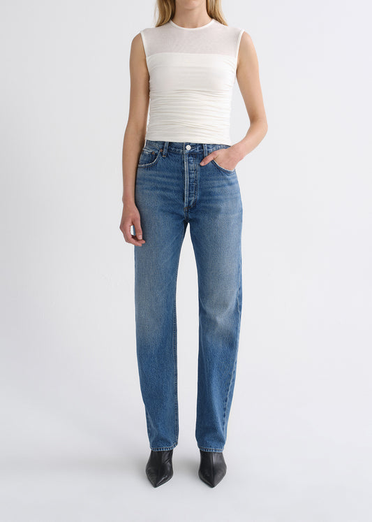 Person wearing white top with blue pants on a grey background