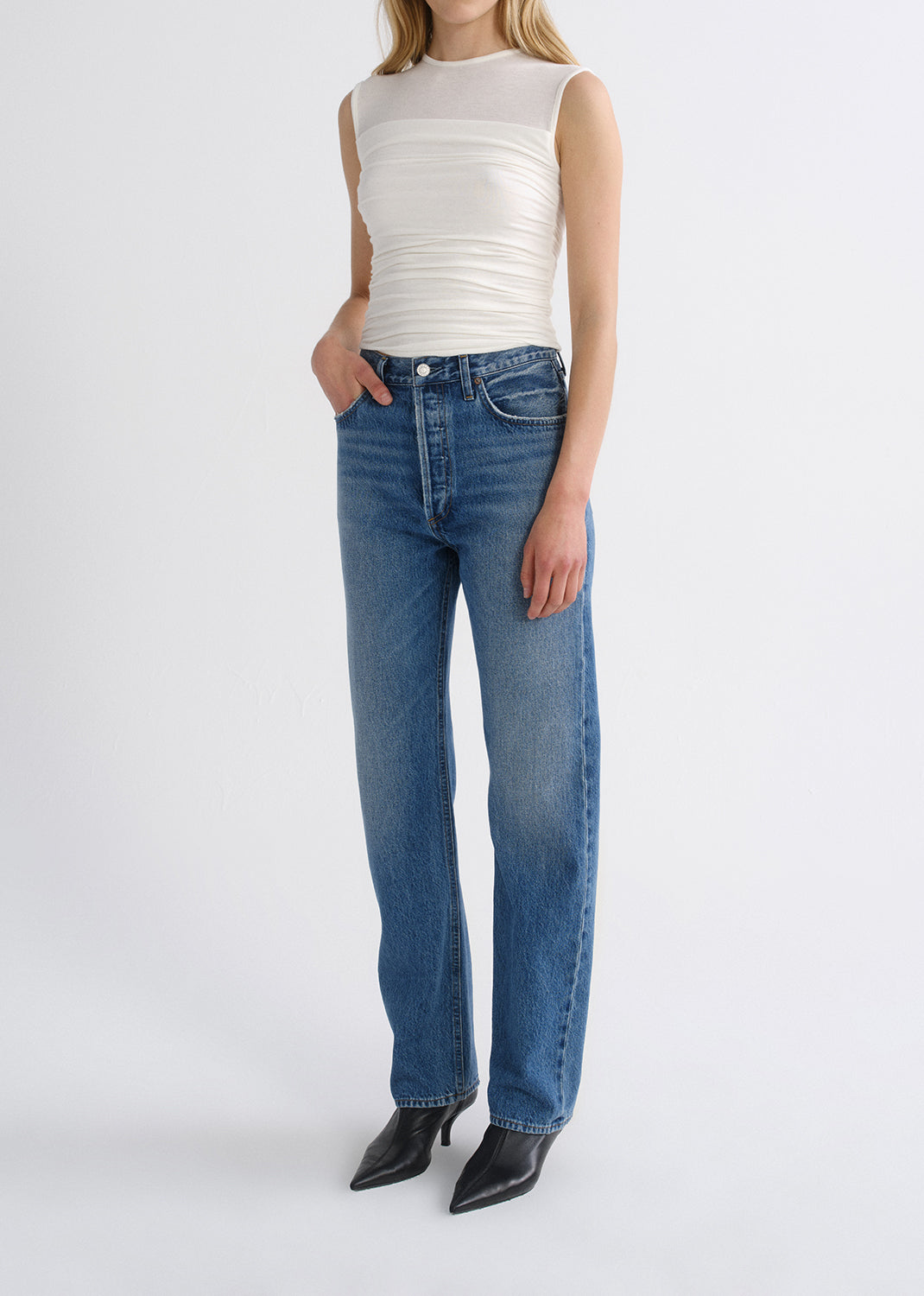 Person wearing white top with blue pants on a grey background