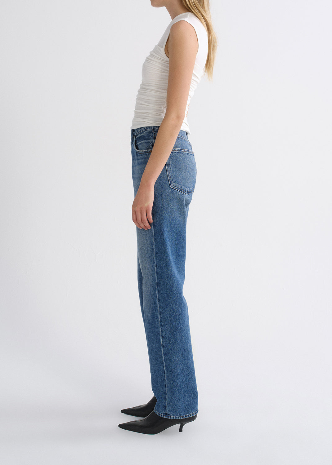 Person wearing white top with blue pants on a grey background