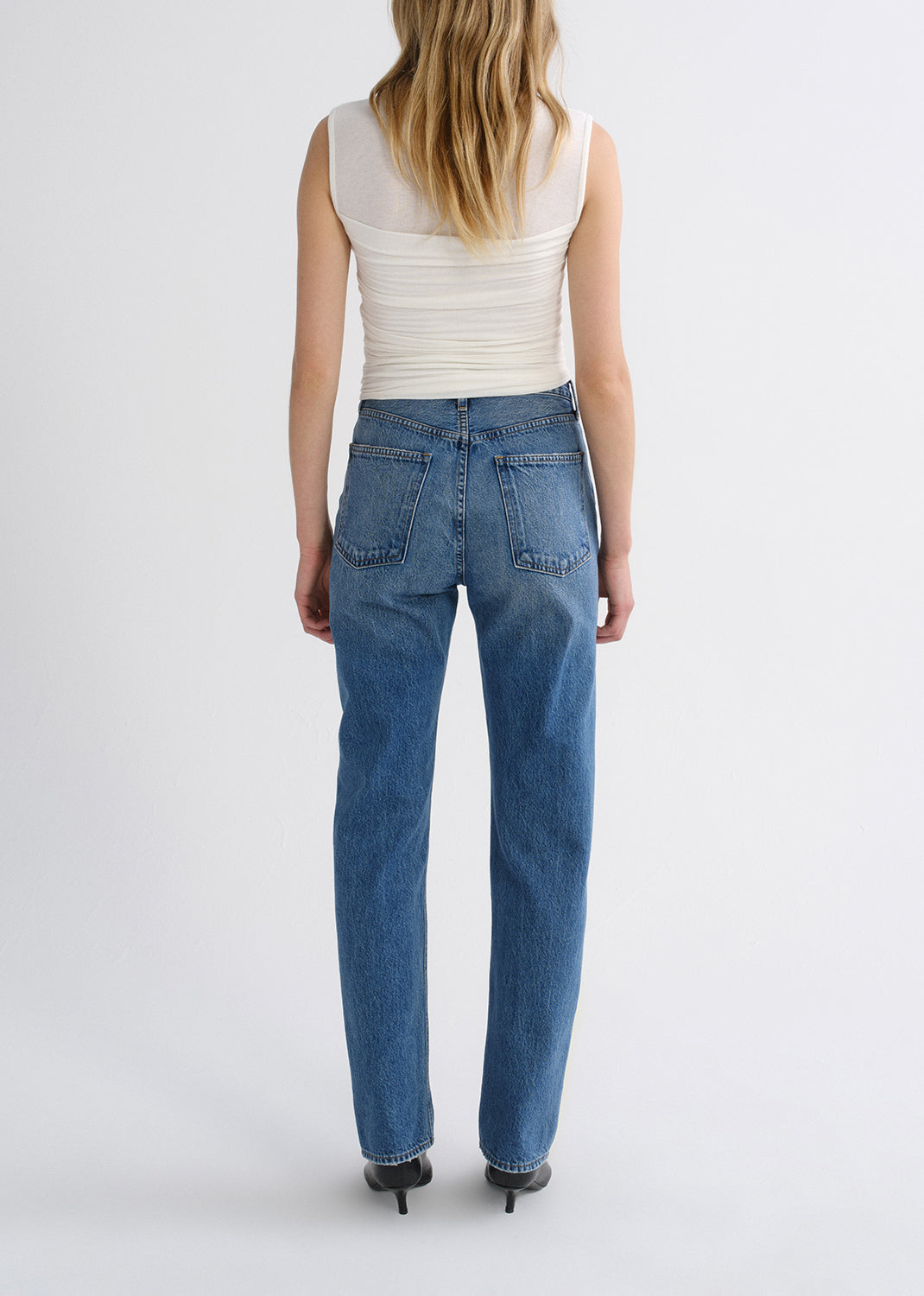Person wearing white top with blue pants on a grey background