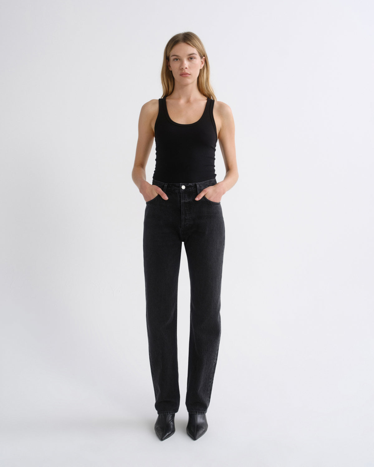 Woman wearing a black tank top with black straight leg pants on a grey background.