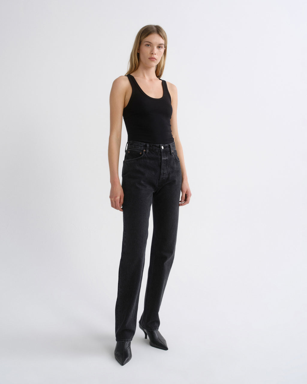 Woman wearing a black tank top with black straight leg pants on a grey background.
