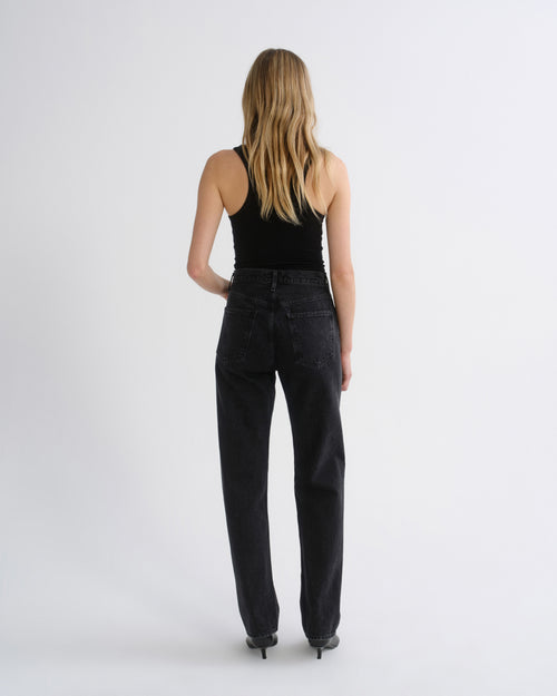 Woman wearing a black tank top with black straight leg pants viewed from the back on a grey background.