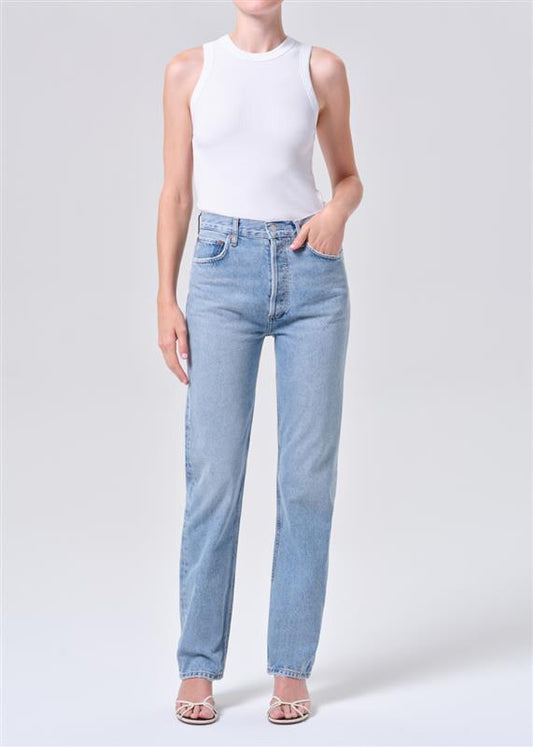 Person wearing light blue jeans and a white sleeveless top on a plain background