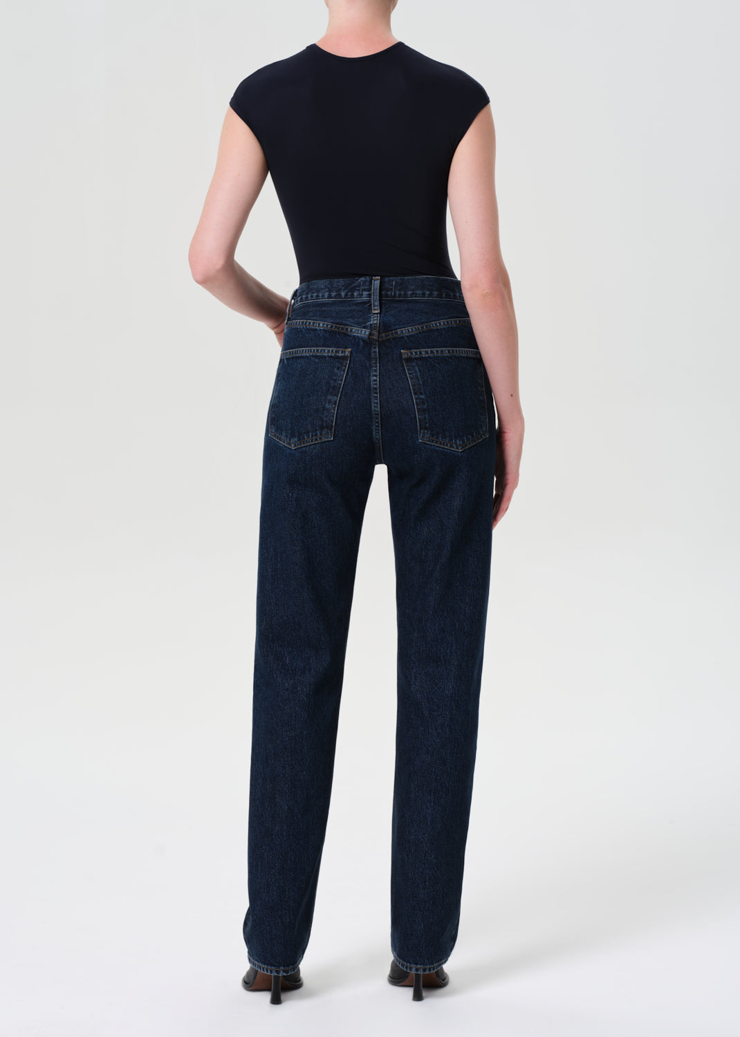 Person wearing dark blue jeans and a black top on a white background