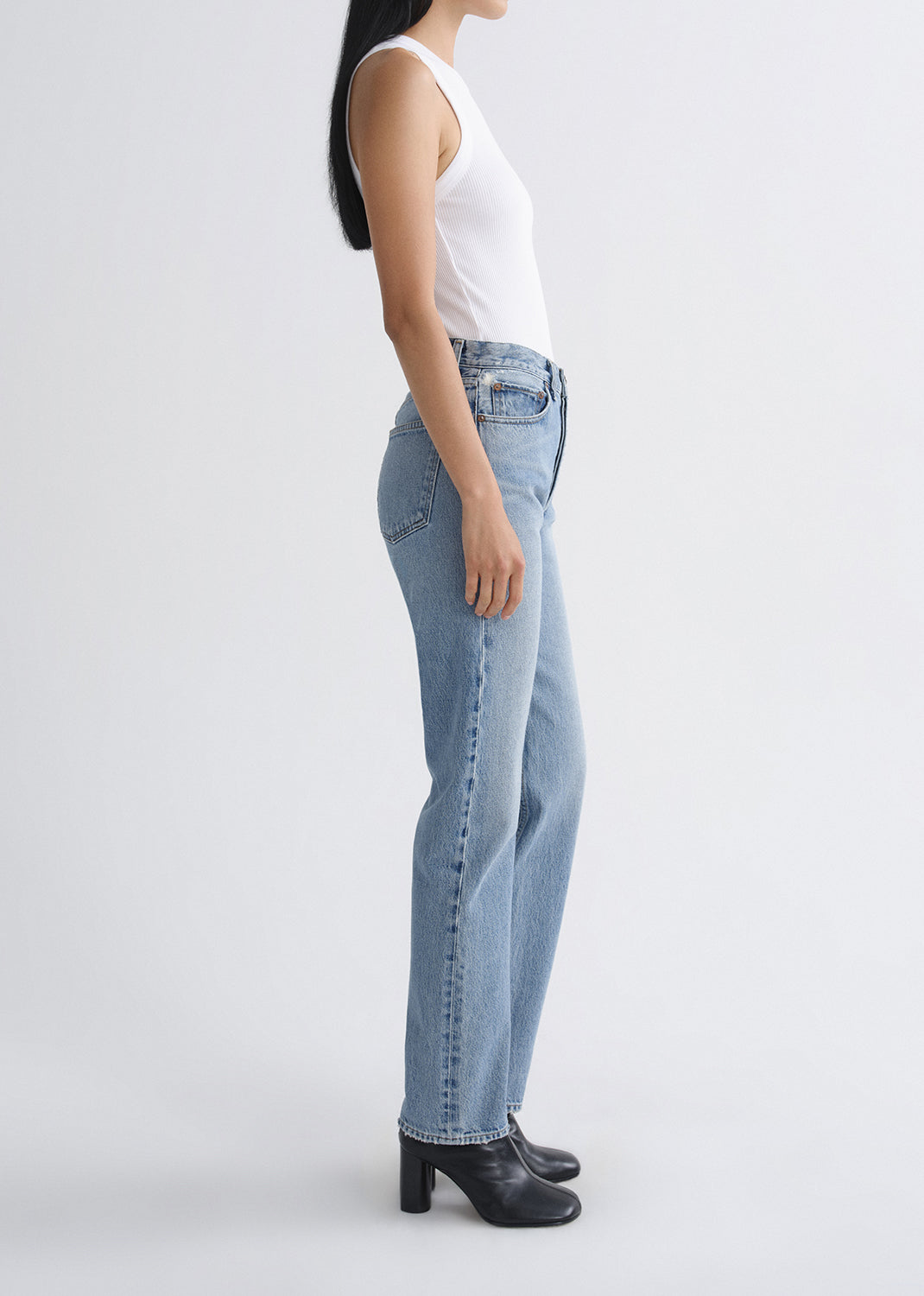 Person wearing light blue jeans and a white top on a grey background