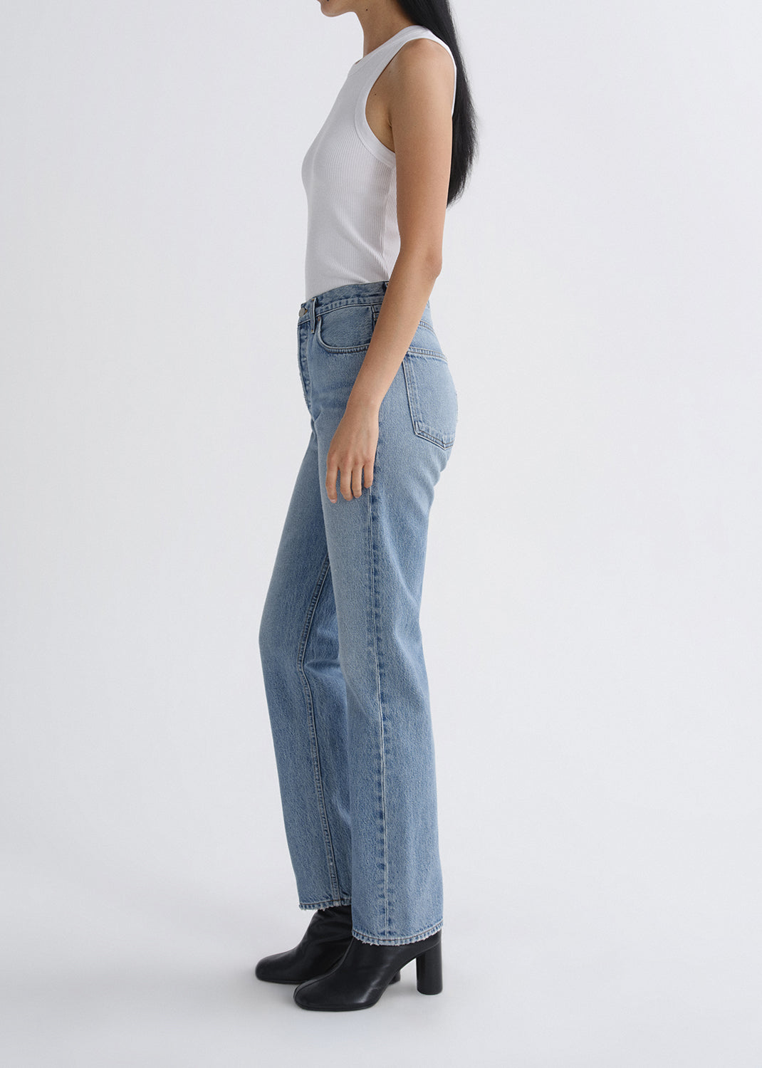 Person wearing light blue jeans and a white top on a grey background