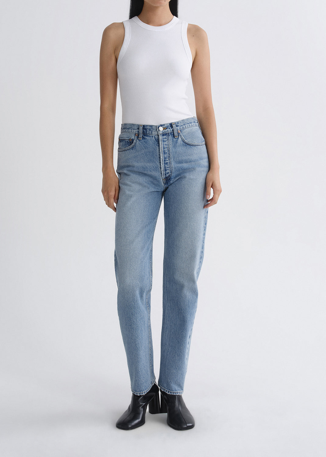 Person wearing light blue jeans and a white top on a grey background