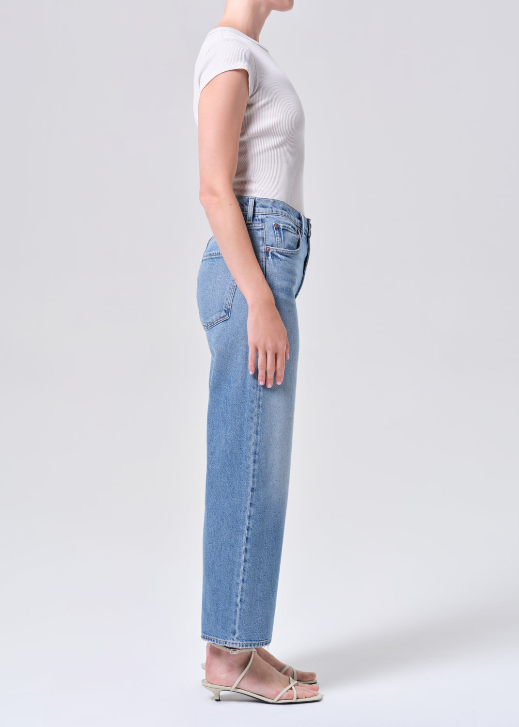 Person wearing light blue jeans and a white top on a plain background