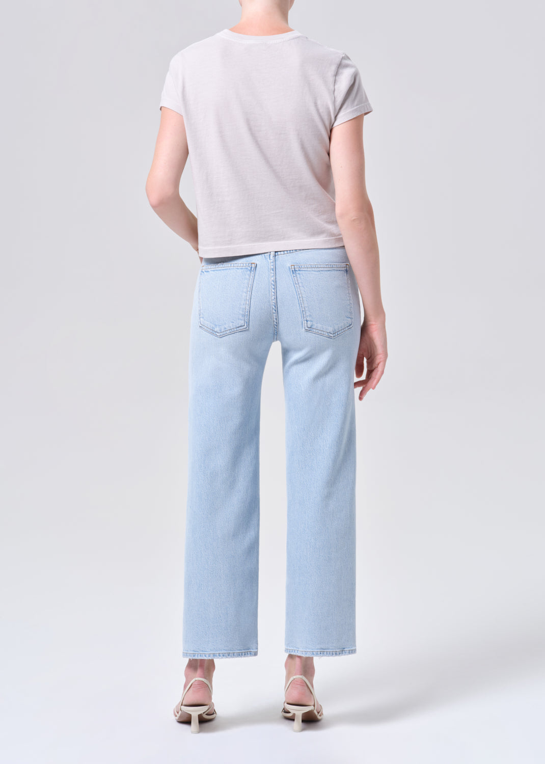 Person wearing light blue jeans and a gray t-shirt on a white background
