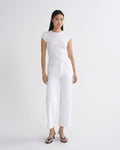 A woman modeling a white short-sleeve crewneck t-shirt and white cropped jeans with black sandals, standing against a solid light gray studio background.