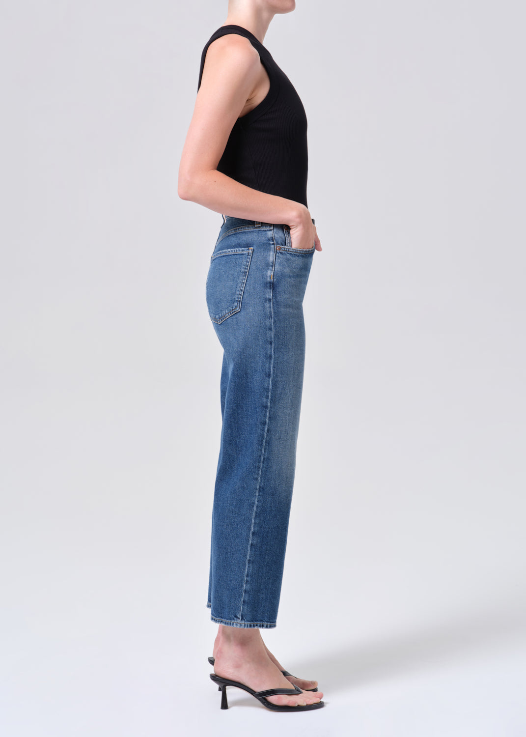 Person wearing blue jeans and a black top on a white background