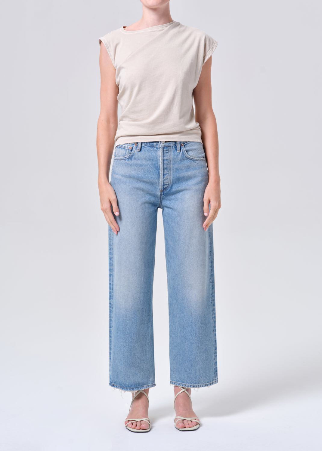 Person wearing a beige top and light blue jeans on a white background