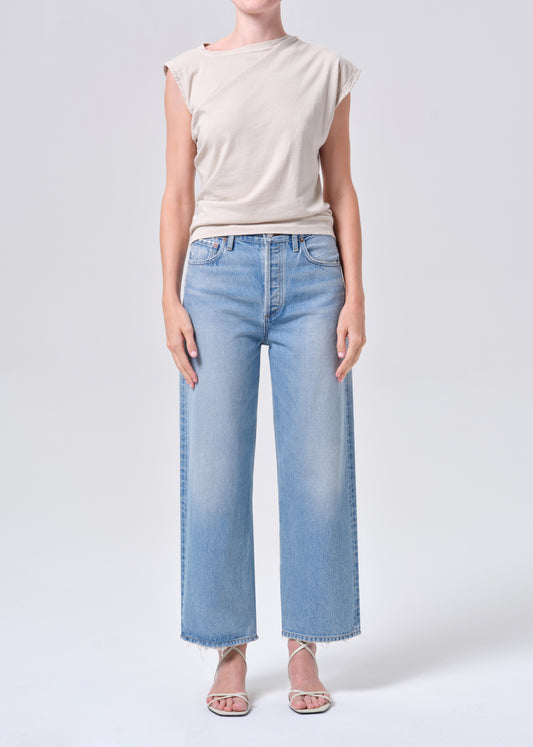 Person wearing a beige top and light blue jeans on a white background