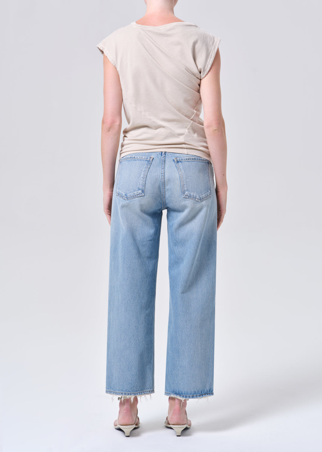 Person wearing light blue jeans and a beige top on a white background