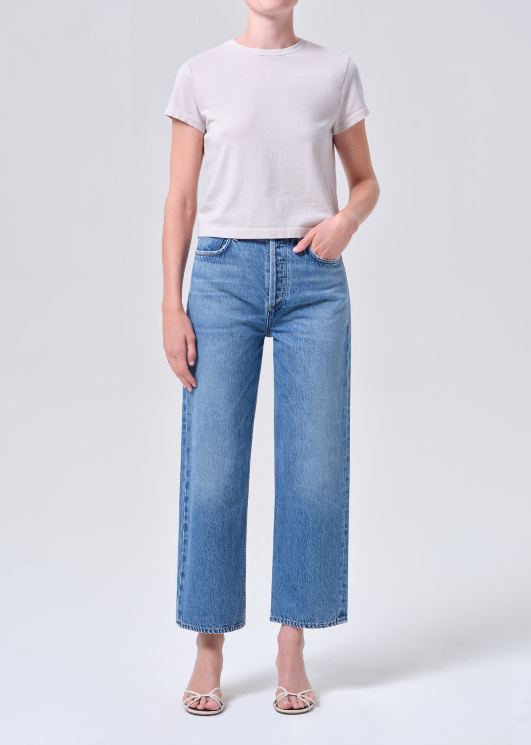 Person wearing a white t-shirt and blue jeans on a light gray background