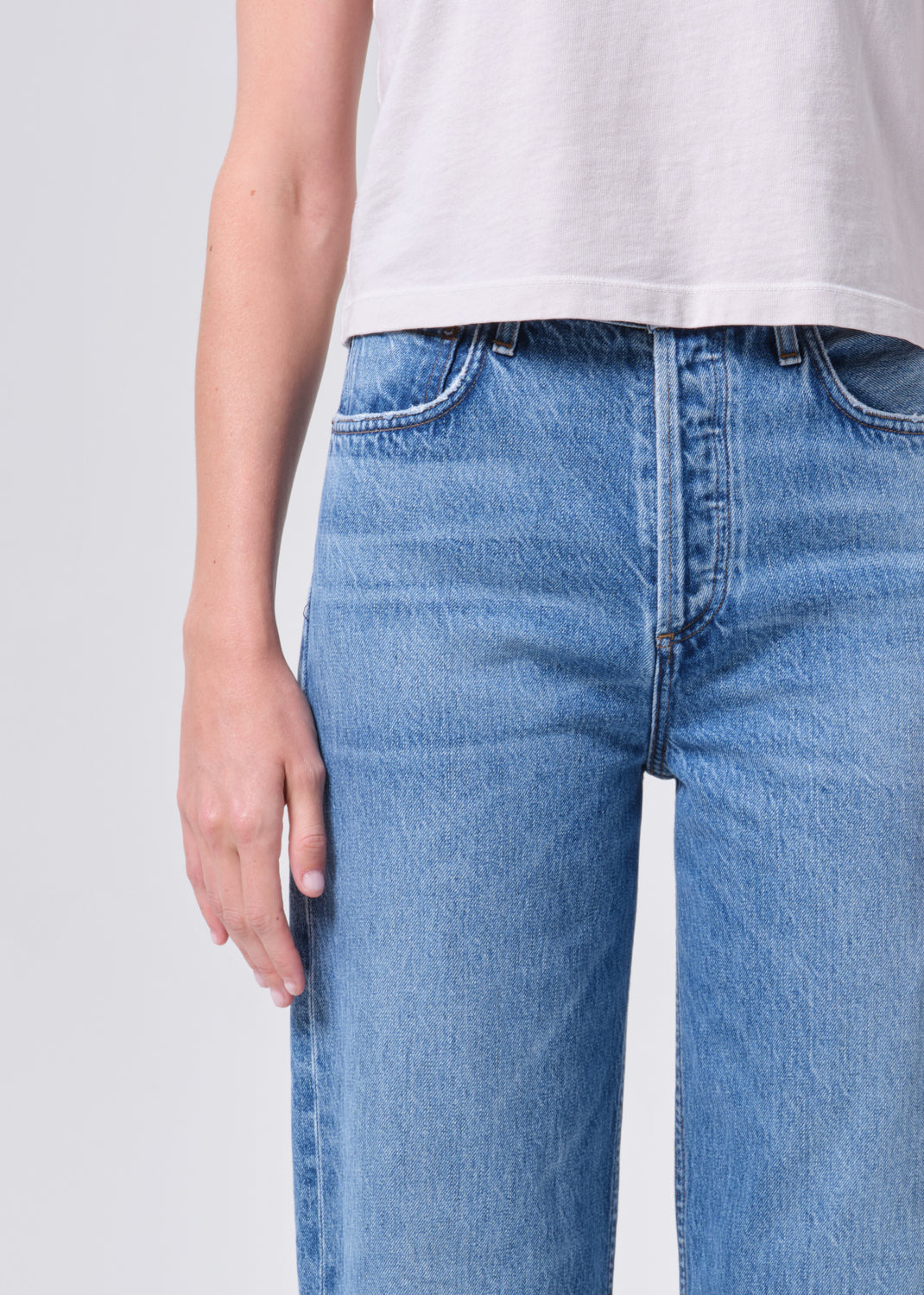 Person wearing light blue jeans and a white shirt on a plain background