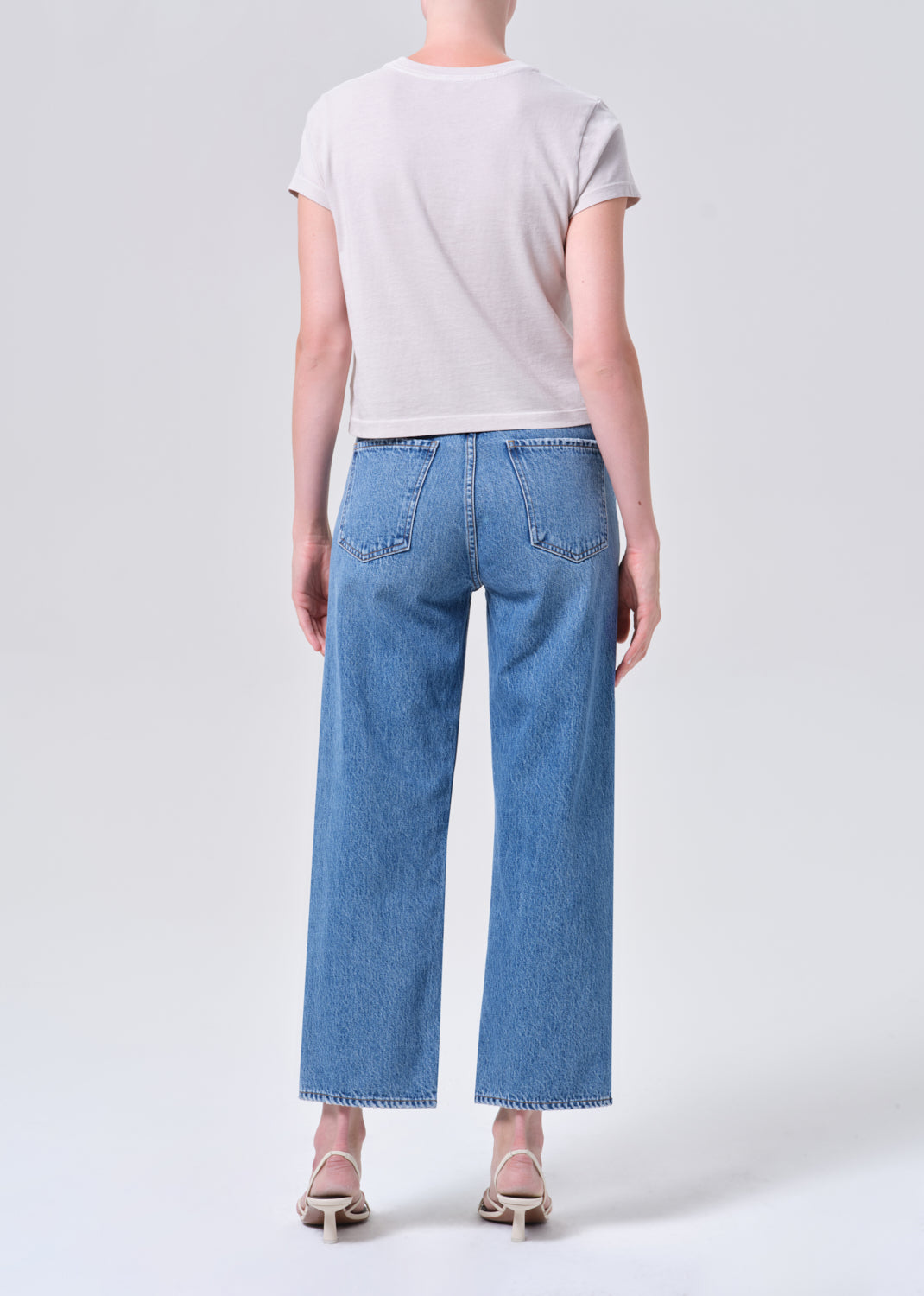 Person wearing a white t-shirt and blue jeans on a plain background