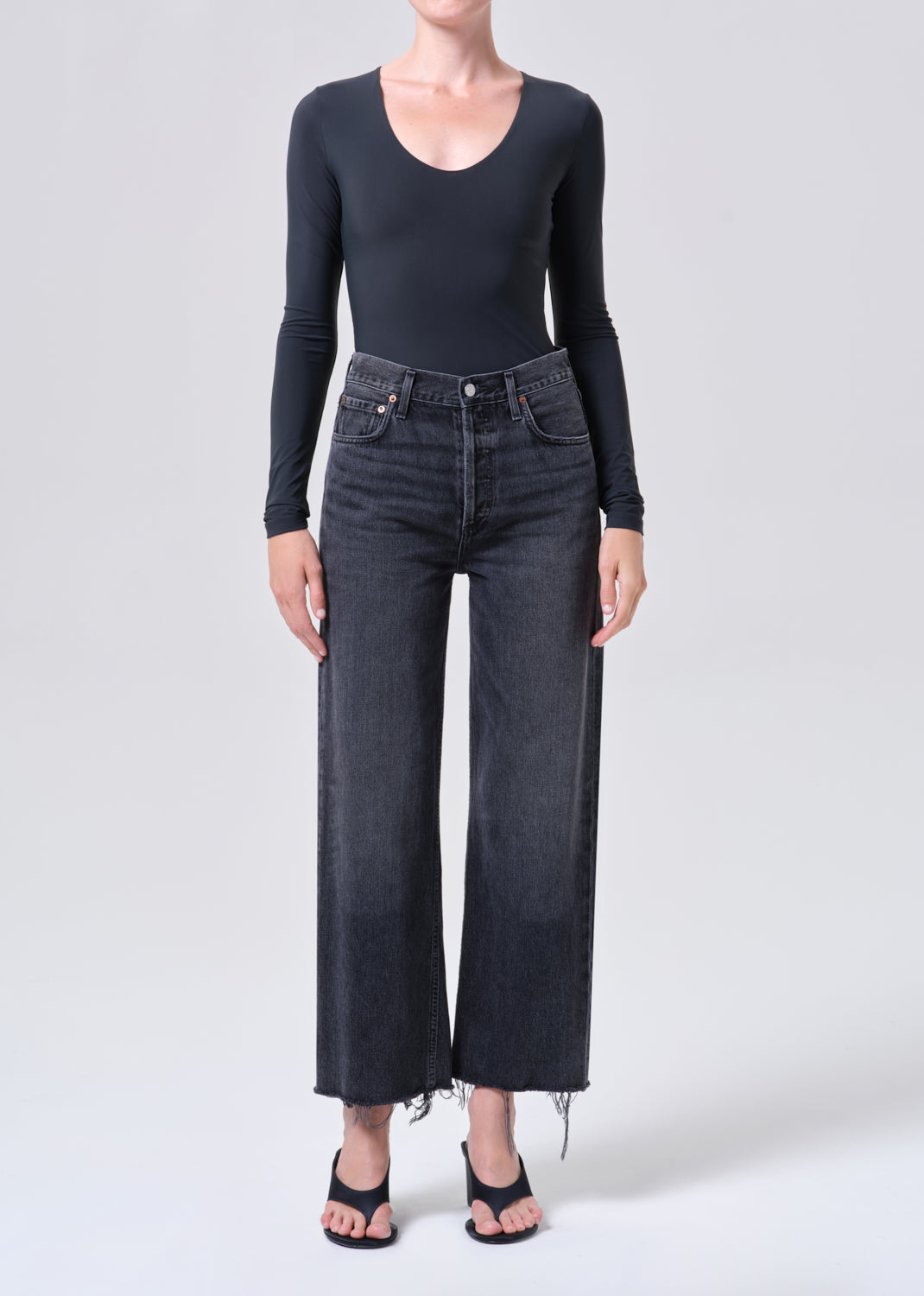 Person wearing a black long-sleeve top and dark jeans on a white background