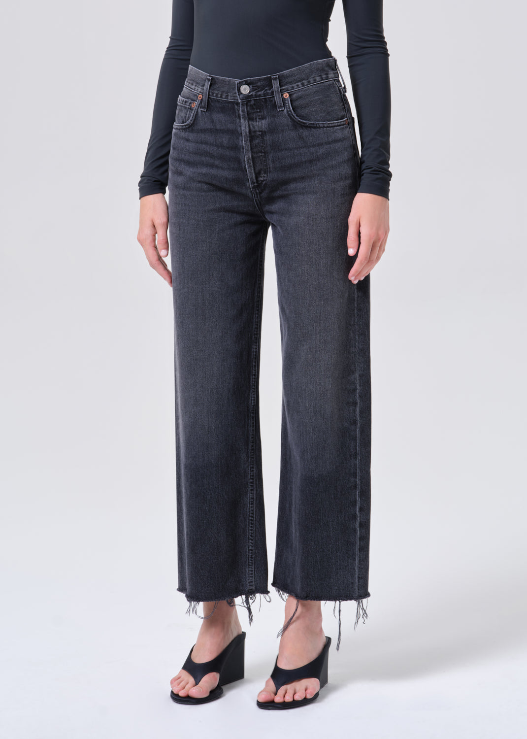 Person wearing black high-waisted jeans and a black long-sleeve top on a white background