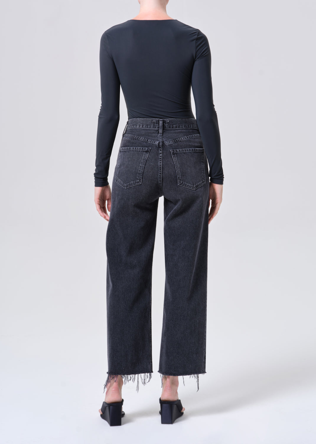 Person wearing black long-sleeve top and dark jeans with fringe details on a white background