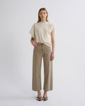A model stands against a light gray studio background wearing a cream-colored sleeveless t-shirt and beige wide-leg cropped pants with black sandals.