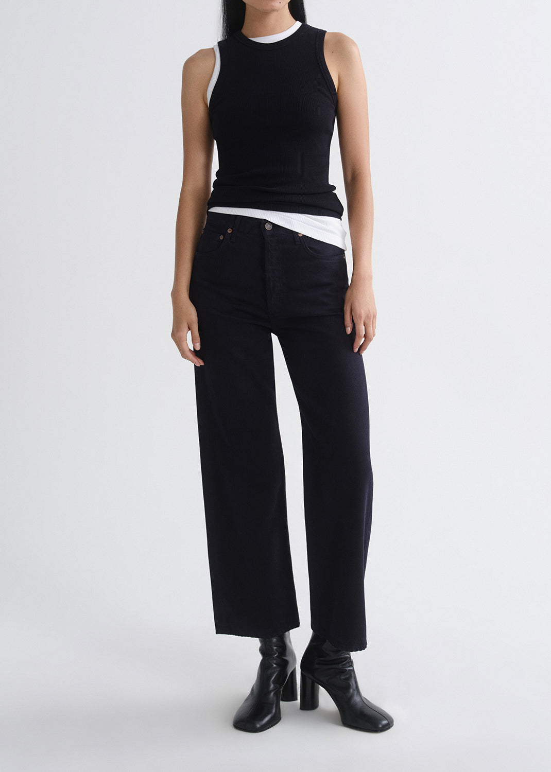 Person wearing a layered black tank and black pants on a grey background