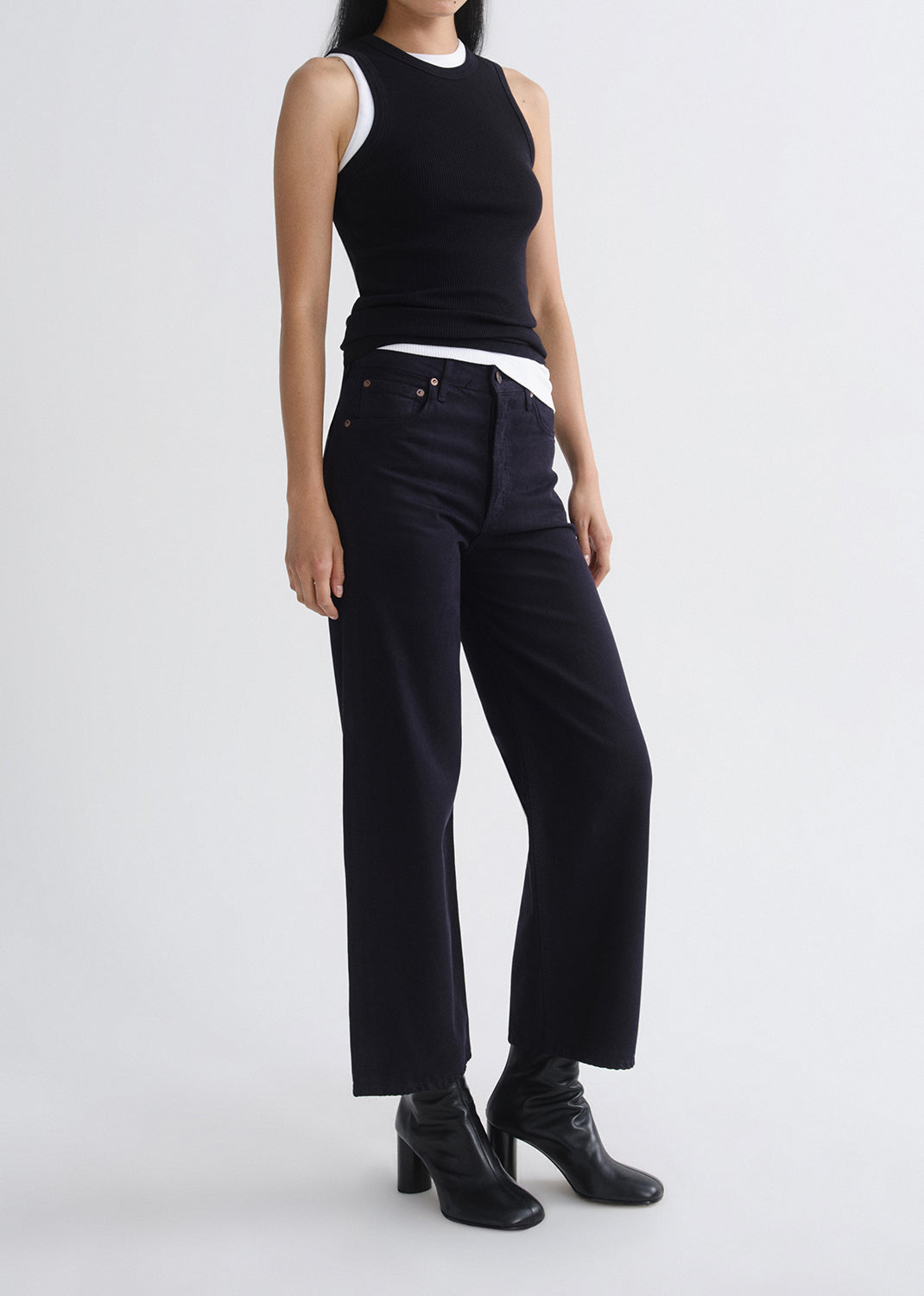Person wearing a layered black tank and black pants on a grey background