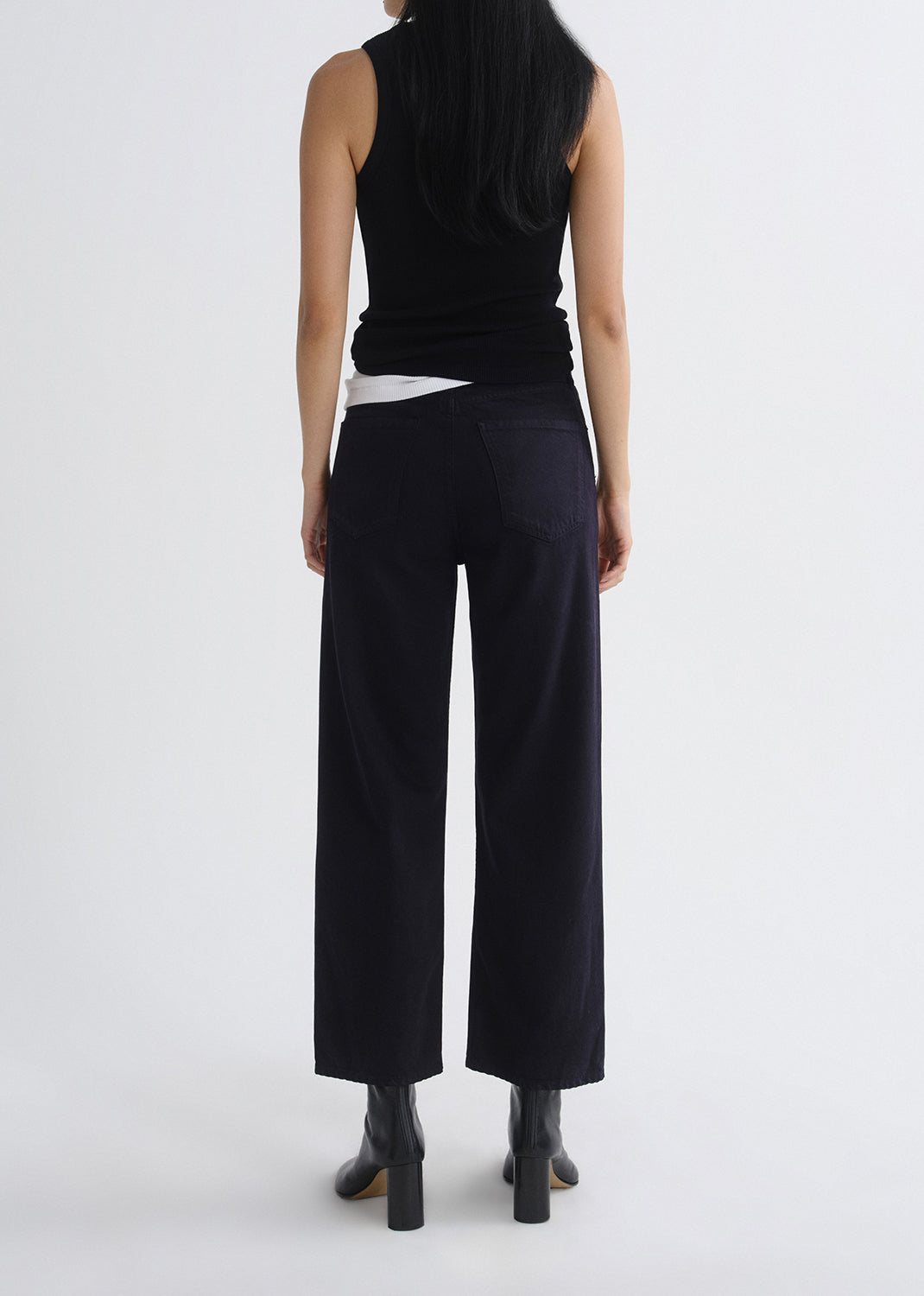 Person wearing a layered black tank and black pants on a grey background