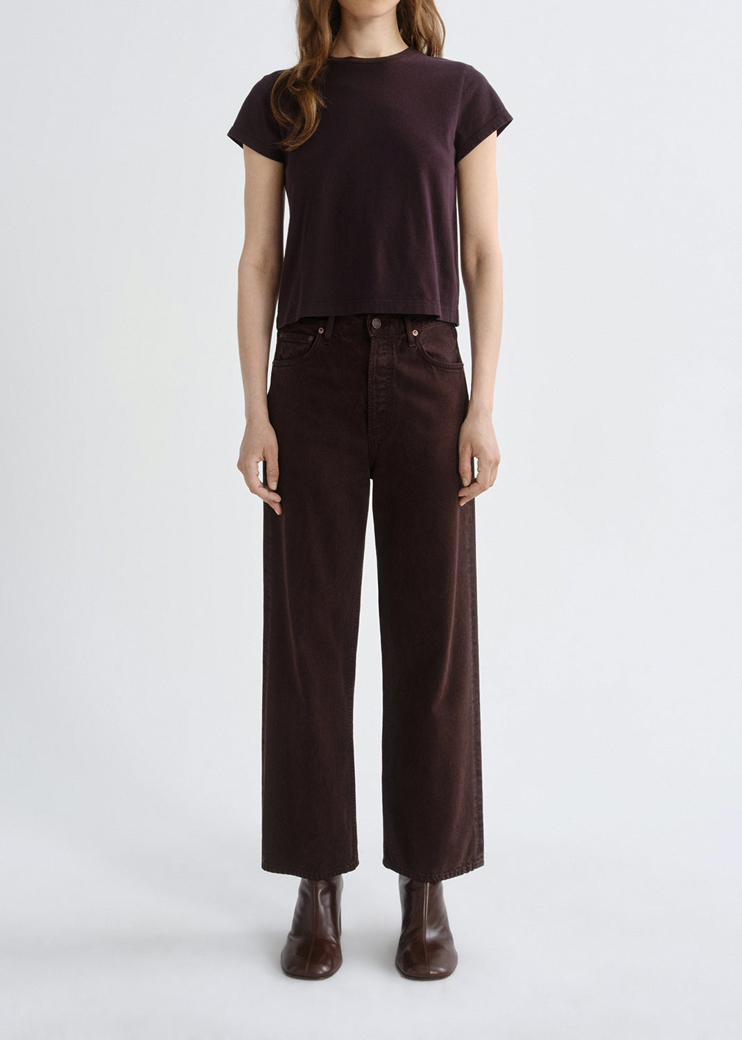 Person wearing a brown t-shirt and dark brown pants on a grey background