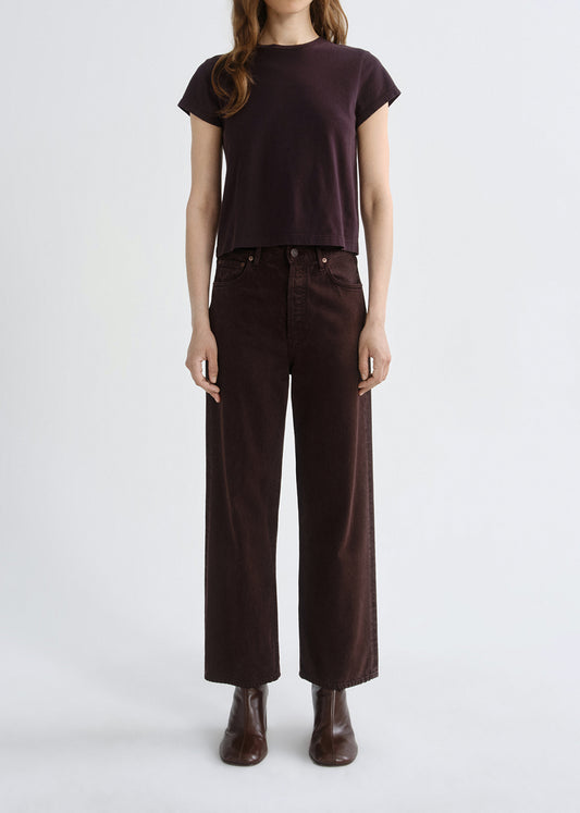 Person wearing a brown t-shirt and dark brown pants on a grey background