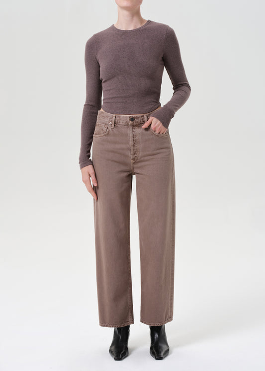 Person wearing a brown long-sleeve top and beige pants on a white background