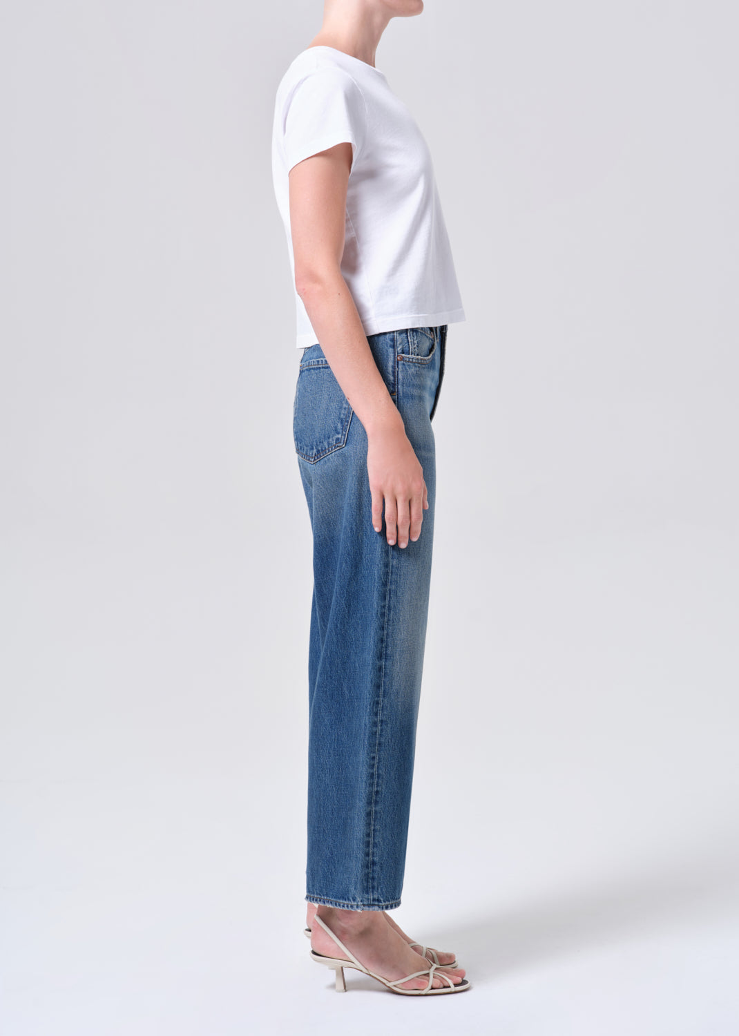 Person wearing a white t-shirt and blue jeans on a plain background