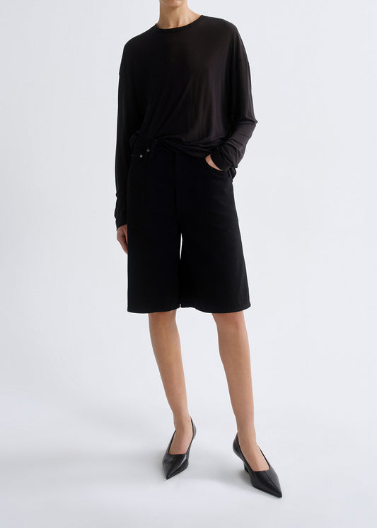 Person wearing a black long-sleeve top and black shorts on a white background