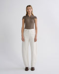 A model stands against a light gray studio background wearing a taupe-brown short-sleeve top with a gathered neckline and white wide-leg jeans.