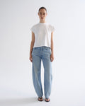 A model stands against a plain light gray studio background wearing a white short-sleeve crew-neck t-shirt and light-wash wide-leg blue jeans with black sandals.
