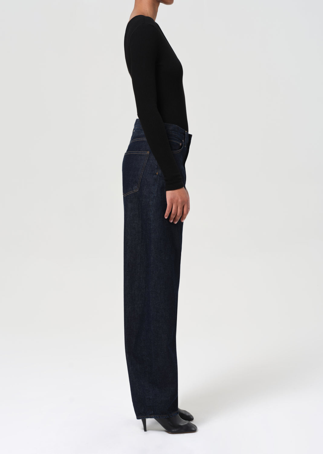 Person wearing dark blue jeans and a black top on a white background