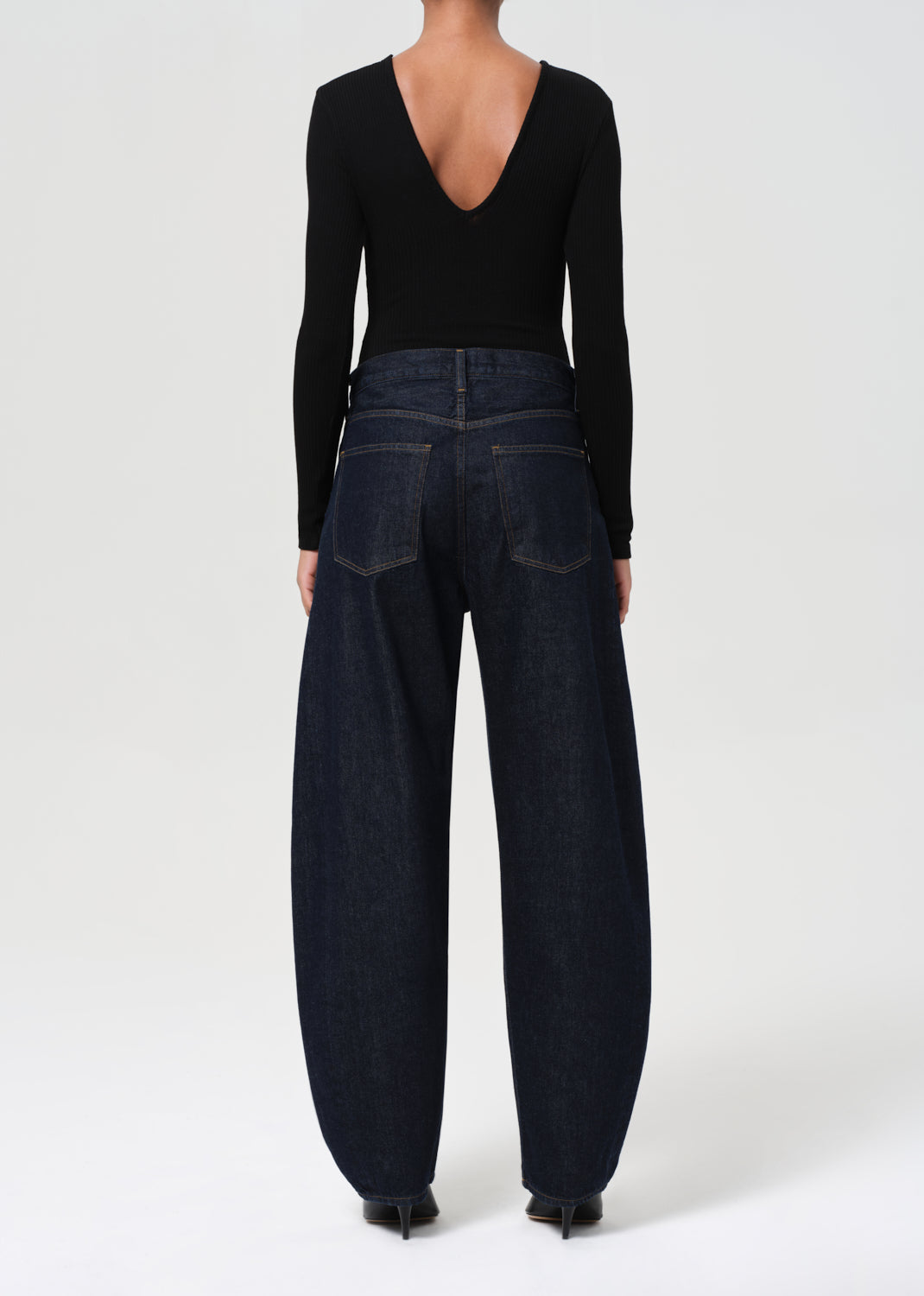 Person wearing a black long-sleeve top and dark blue jeans on a white background