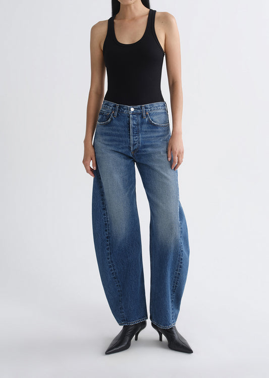 Person wearing blue jeans and a black tank top on a grey background