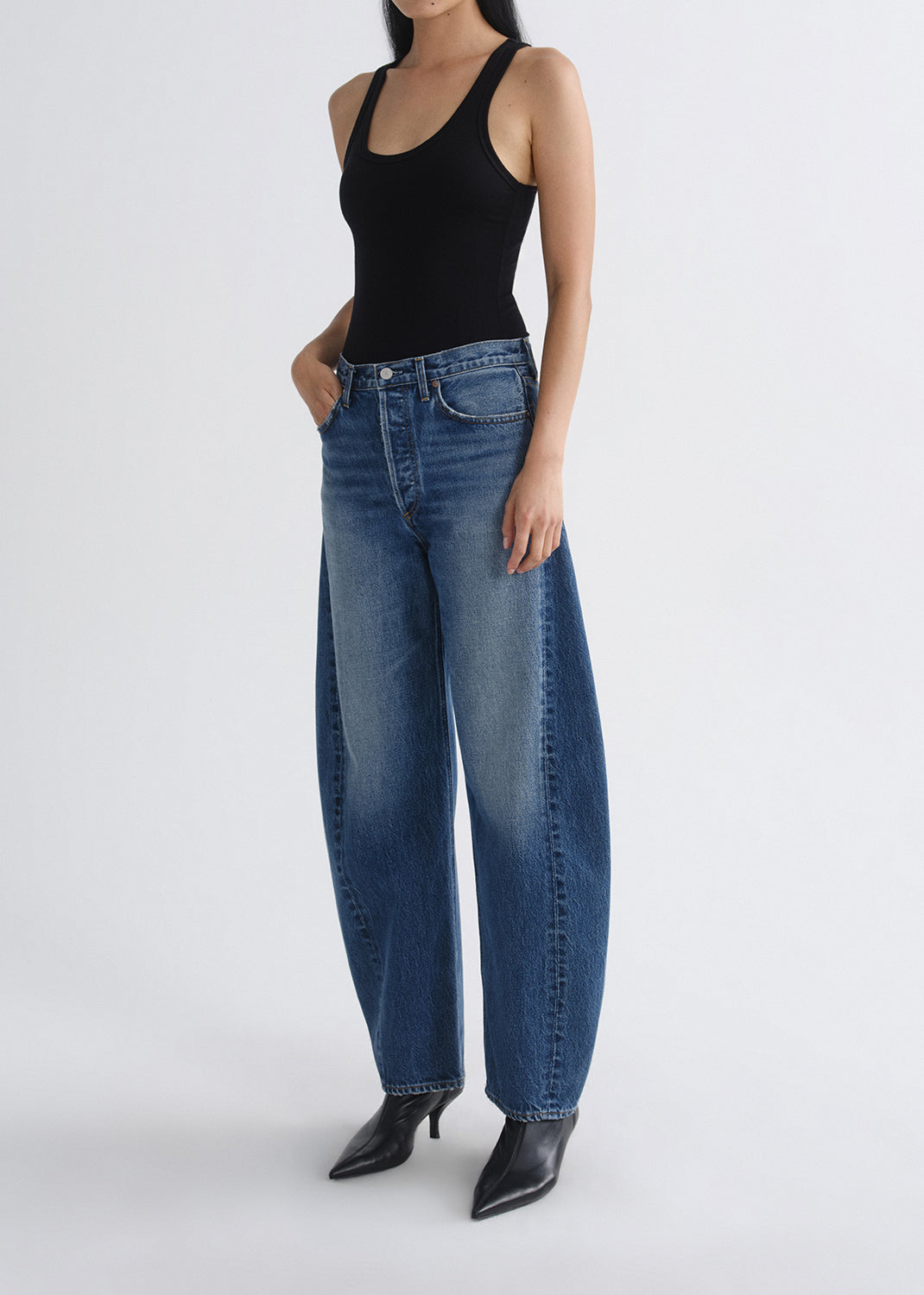Person wearing a black tank top and blue jeans on a grey background