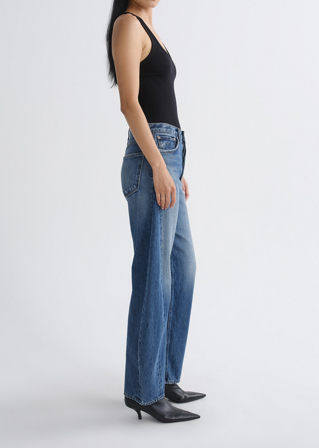 Person wearing blue jeans and black high-heeled shoes on a grey background