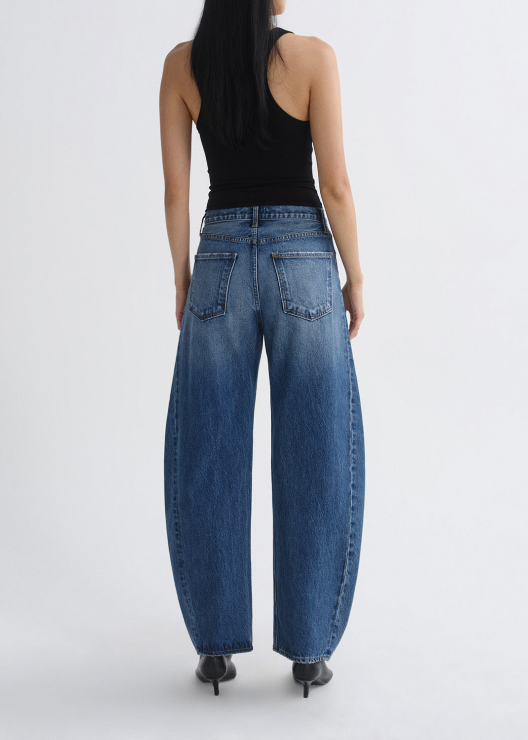 Person wearing blue jeans and a black top on a grey background