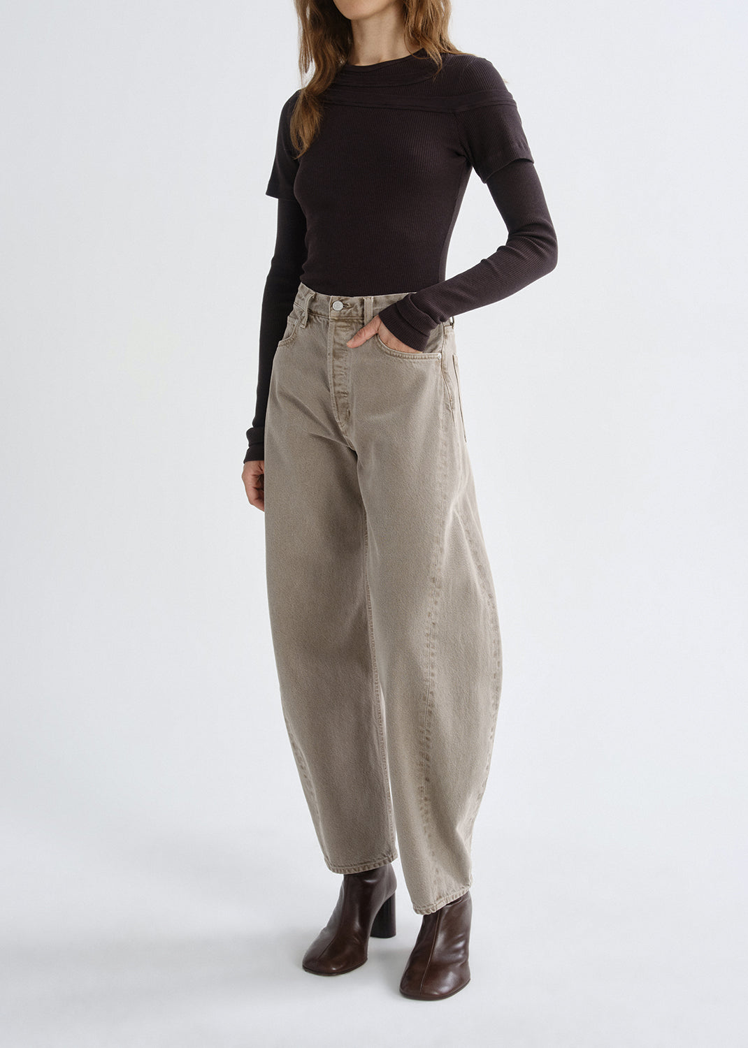 Person wearing a black long-sleeve top and beige high-waisted pants on a grey background