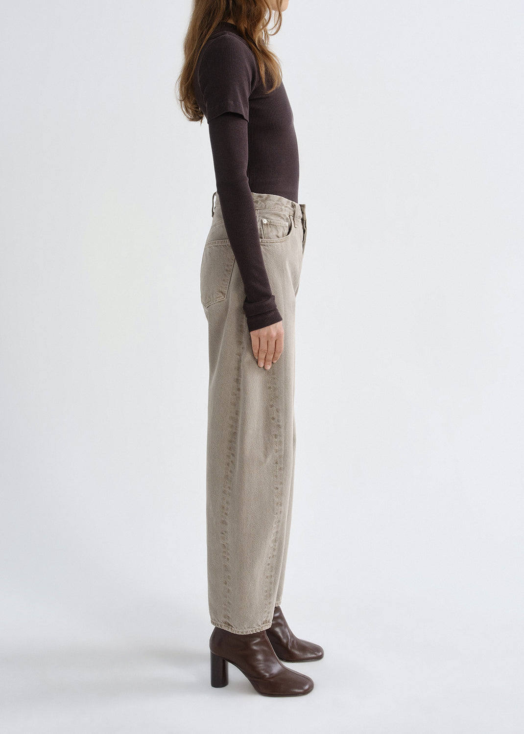 Person wearing beige wide-leg jeans and brown shoes on a grey background
