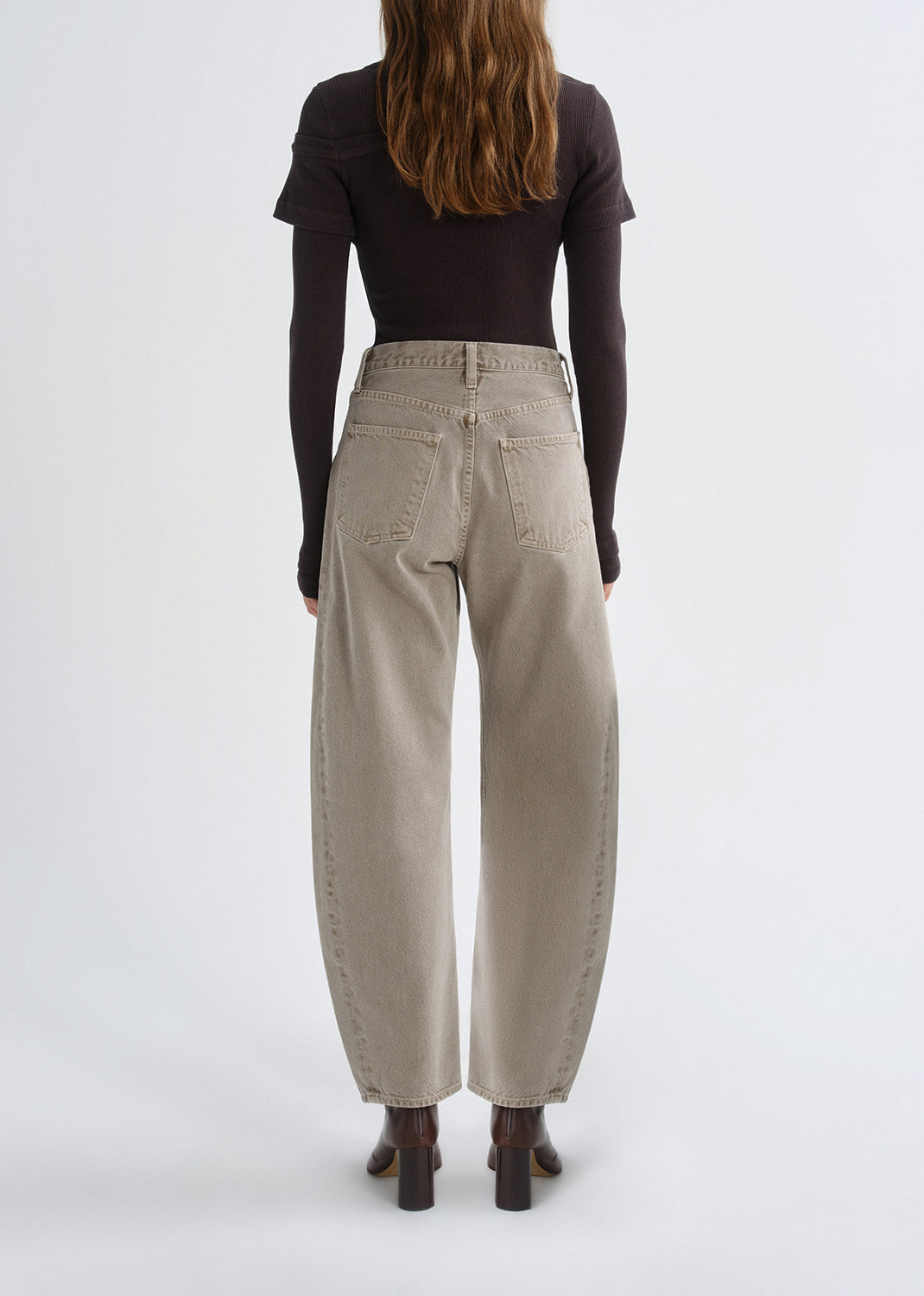 Person wearing beige pants and a black top on a grey background