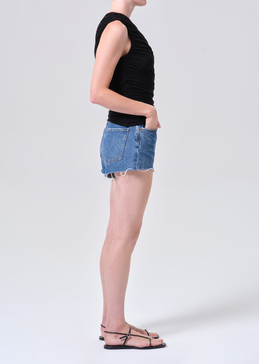 Person wearing a black sleeveless top and blue denim shorts on a white background